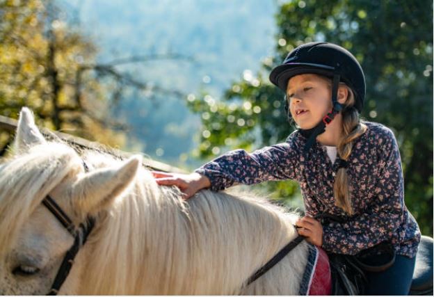 Jeune enfant, casque sur la tête, monté sur un poney dun en piste sablée avec un moniteur