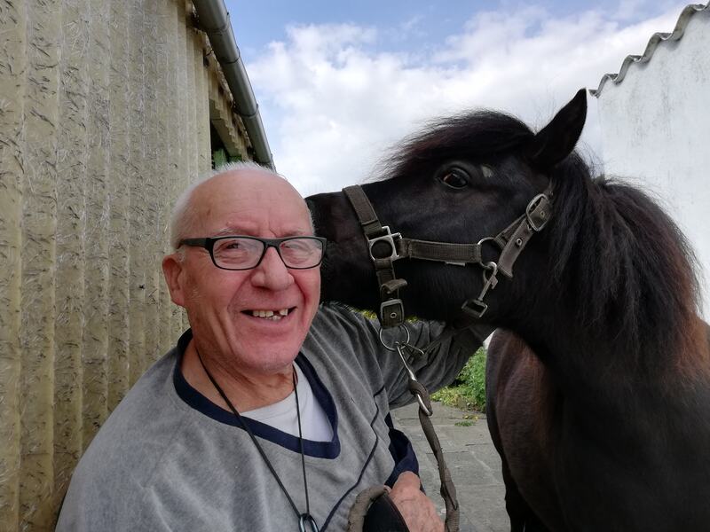 Monsieur d'âge mûr souriant avec un poney noir qui lui murmure à l'oreille